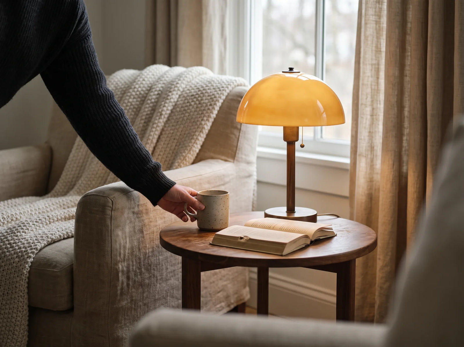 Une main posant une tasse à côté d'une lampe de table allumée dans un coin lecture