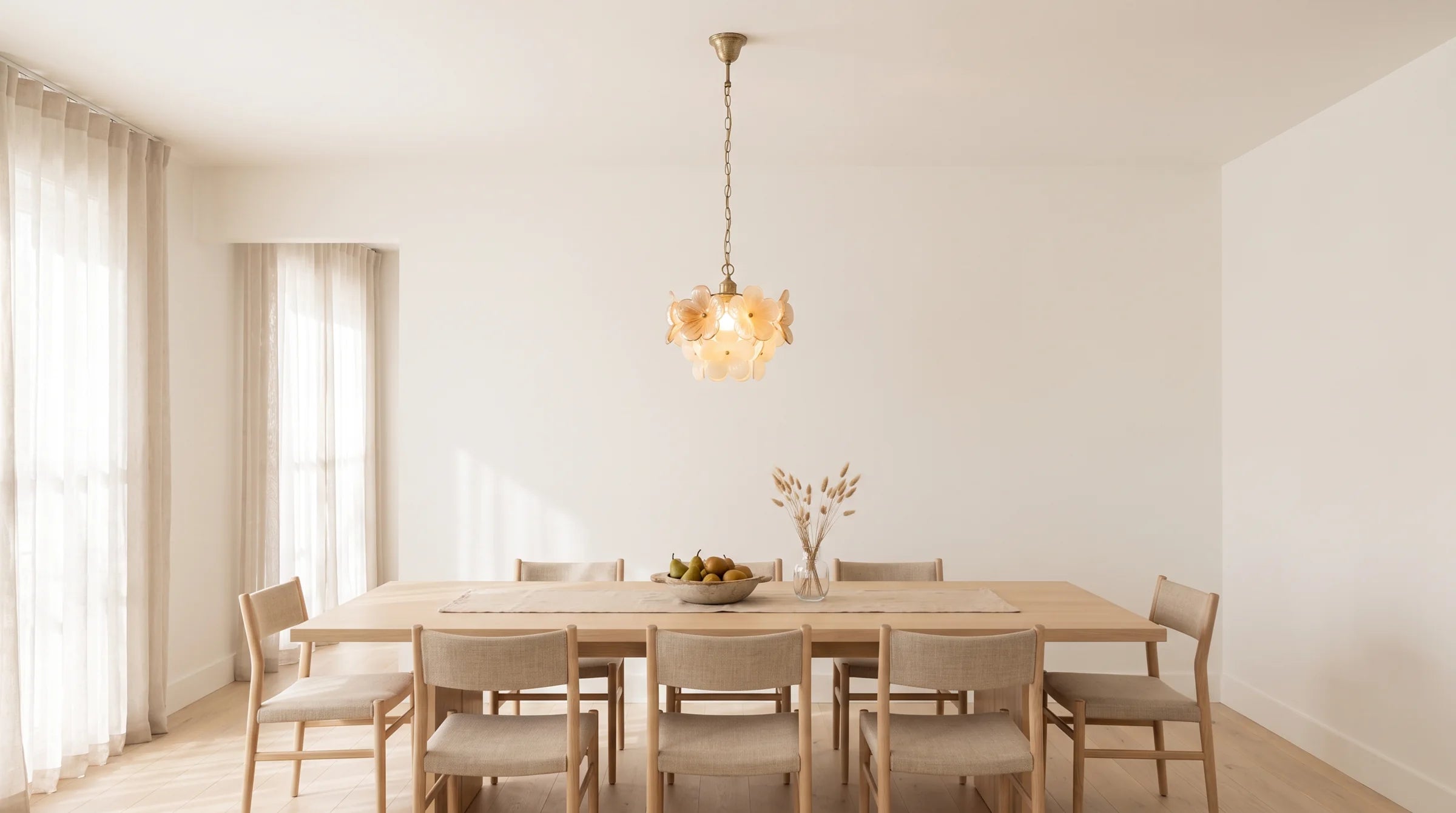 Une table à manger en chêne pâle sous une suspension florale en verre baignée par la lumière du matin